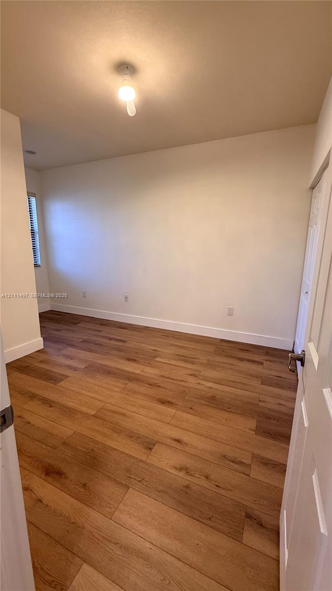 Interior room featuring wood-finish flooring, neutral wall tones, a window with horizontal blinds, and a built-in closet