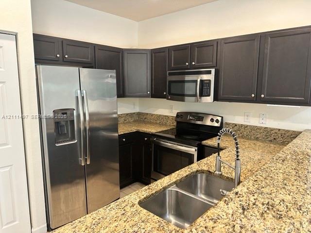 Kitchen featuring dark-finish cabinetry, stone-composite countertops, stainless steel appliances, a double-basin under-mount sink, and a gooseneck pull-down faucet