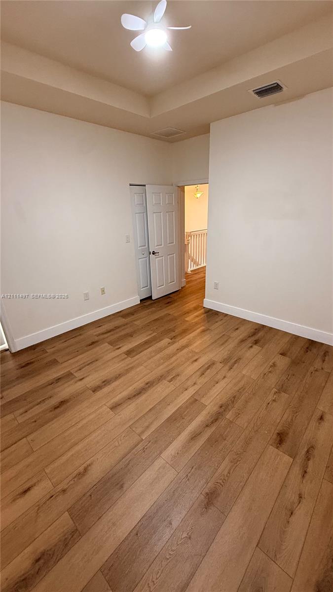 Room featuring wood-finish flooring, tray ceiling, dual-panel interior closet doors, and a ceiling fan with integrated lighting