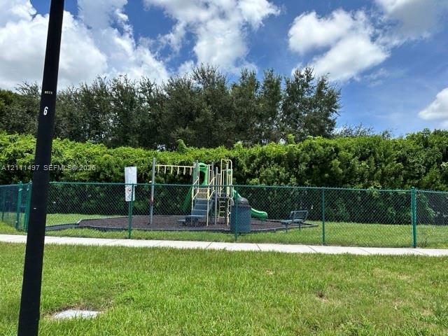 Outdoor recreation area featuring a playground structure with a slide, chain-link perimeter fencing, and mature hedge landscaping