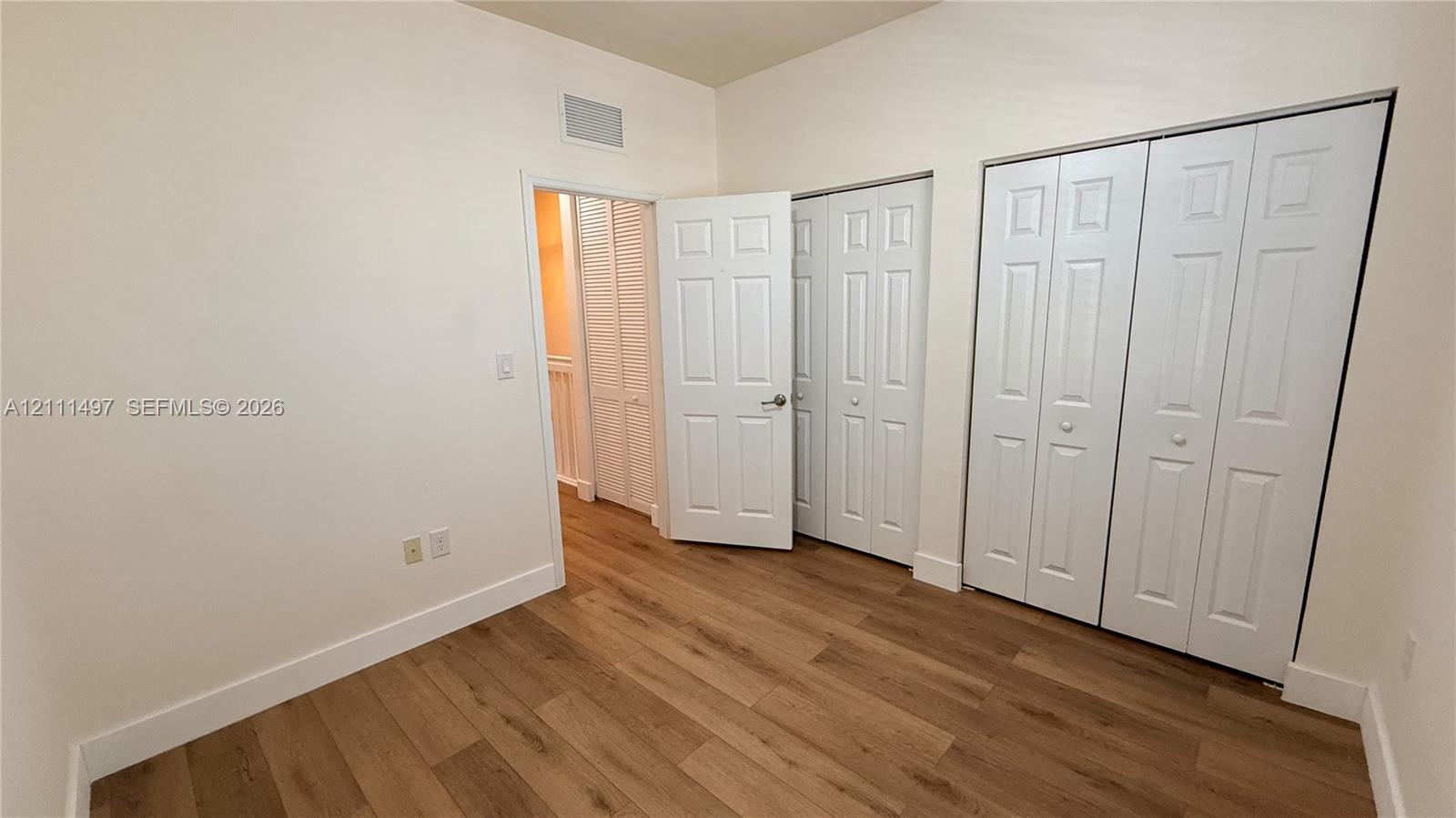 Interior room featuring wood-finish flooring, six-panel interior doors, and double-door closet storage