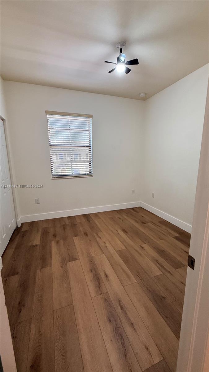 Interior space featuring wood-finish flooring, a neutral wall palette, a single window with horizontal blinds, and a central ceiling fan with an integrated light fixture