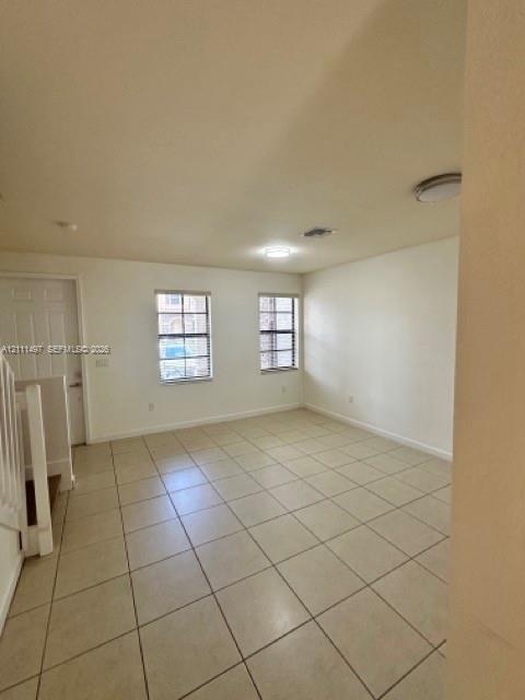 Open interior space featuring light-toned tile flooring, two double-hung windows with horizontal blinds, neutral wall finishes, and flush-mount ceiling lighting