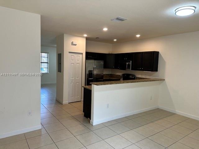 Kitchen featuring dark cabinetry, stone-finish countertops, stainless steel appliances, a breakfast bar, and tile flooring