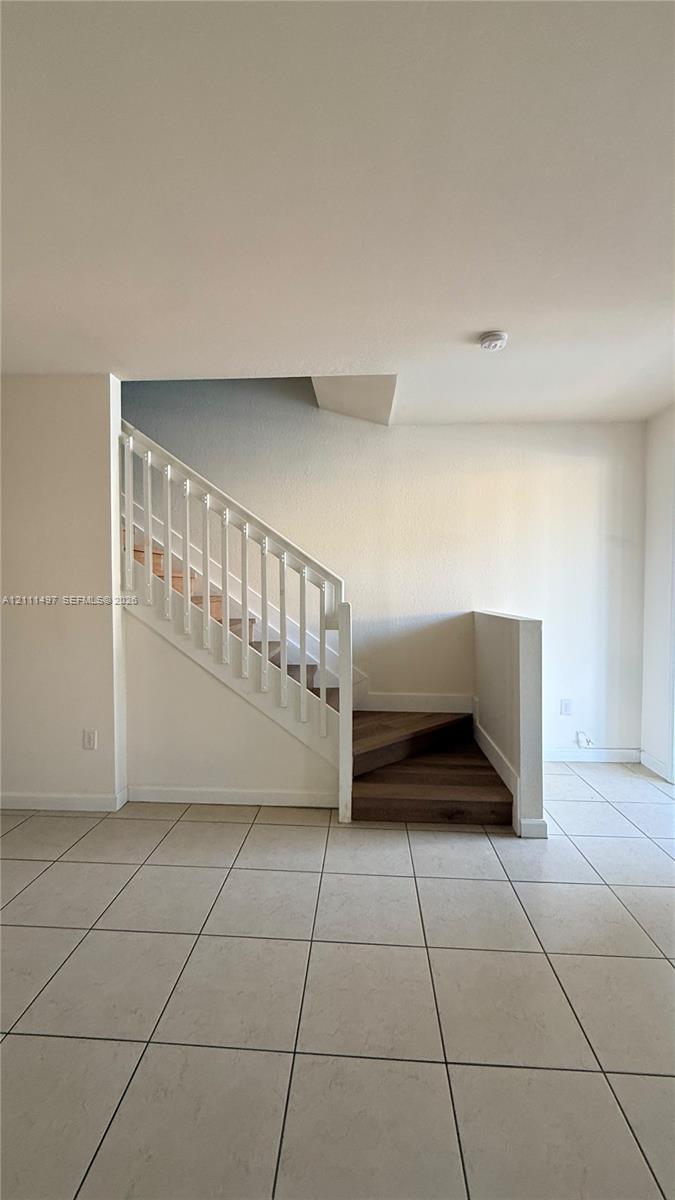 Staircase featuring white balusters, wood-finish treads, and neutral tile flooring