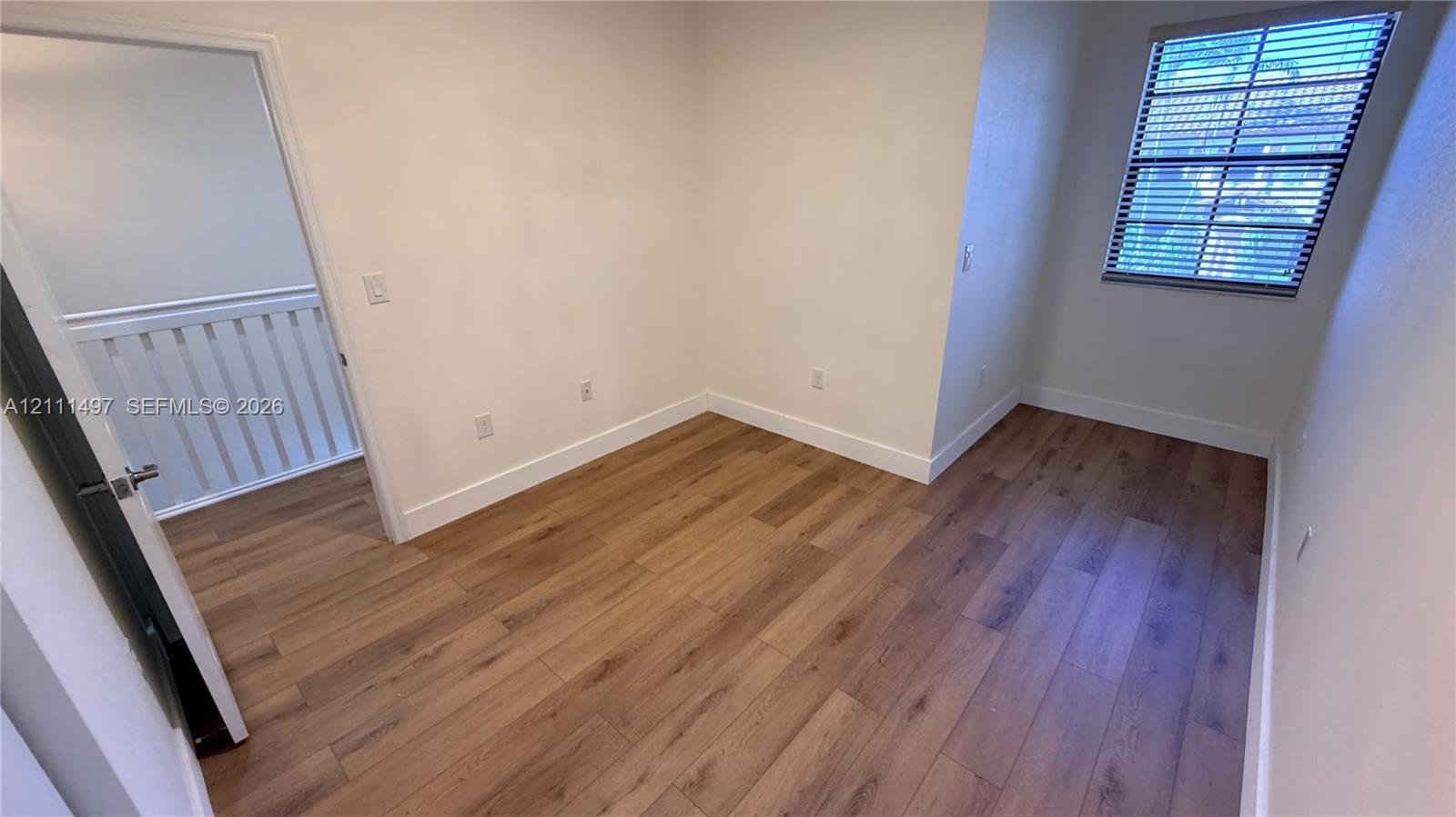 Room featuring wood-finish flooring, neutral wall paint, and a single-pane window with installed blinds