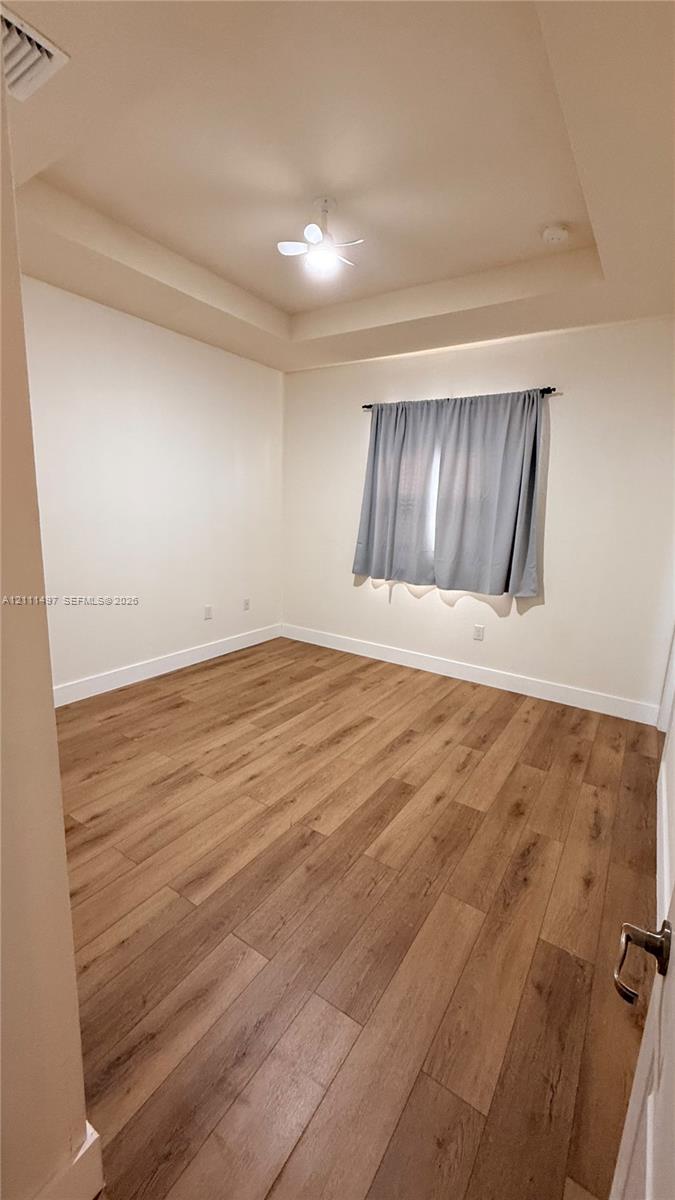 Tray ceiling featuring a recessed center, wood-finish flooring, and a central ceiling fan with an integrated light fixture