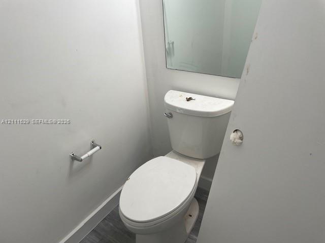 Restroom featuring a wall-mounted mirror, white elongated toilet, and wood-finish flooring