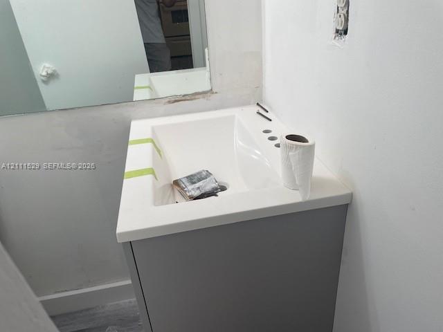 Single-sink vanity featuring a solid-surface countertop with an integrated basin and a neutral grey cabinet base, paired with a wall-mounted rectangular mirror