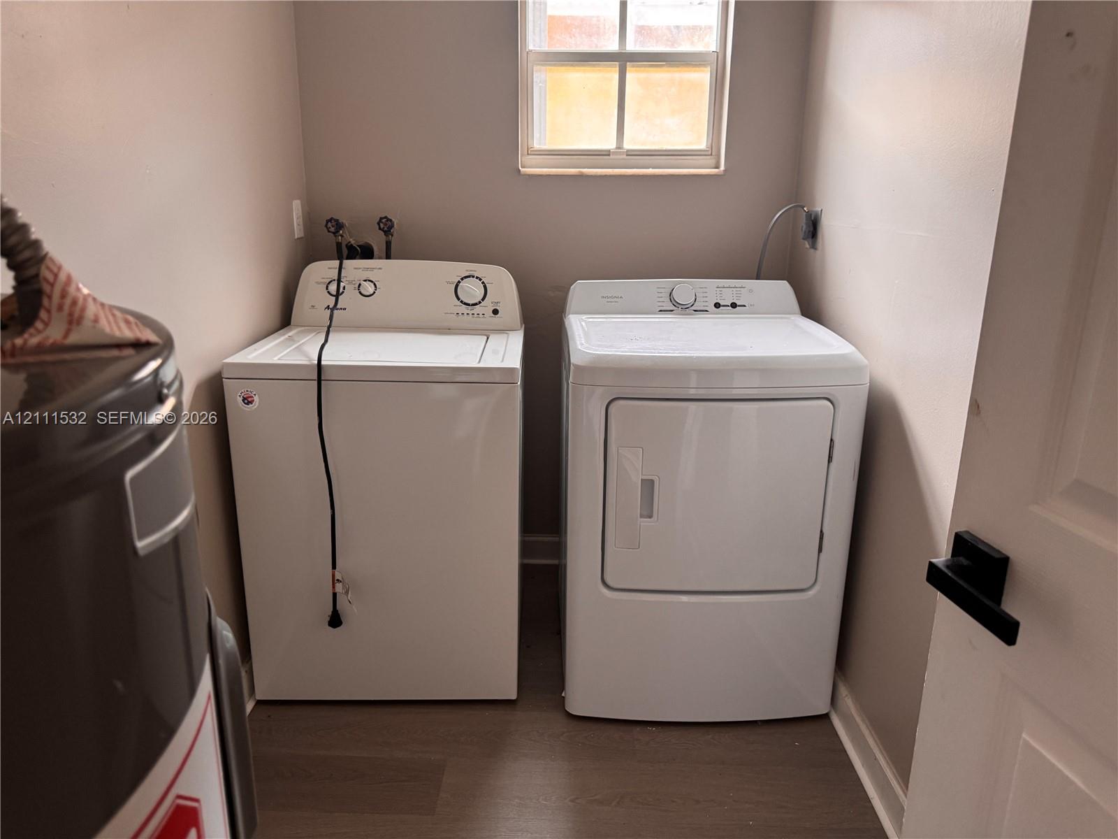 Dedicated laundry space featuring wood-finish flooring, a window, and a white interior door with matte black hardware