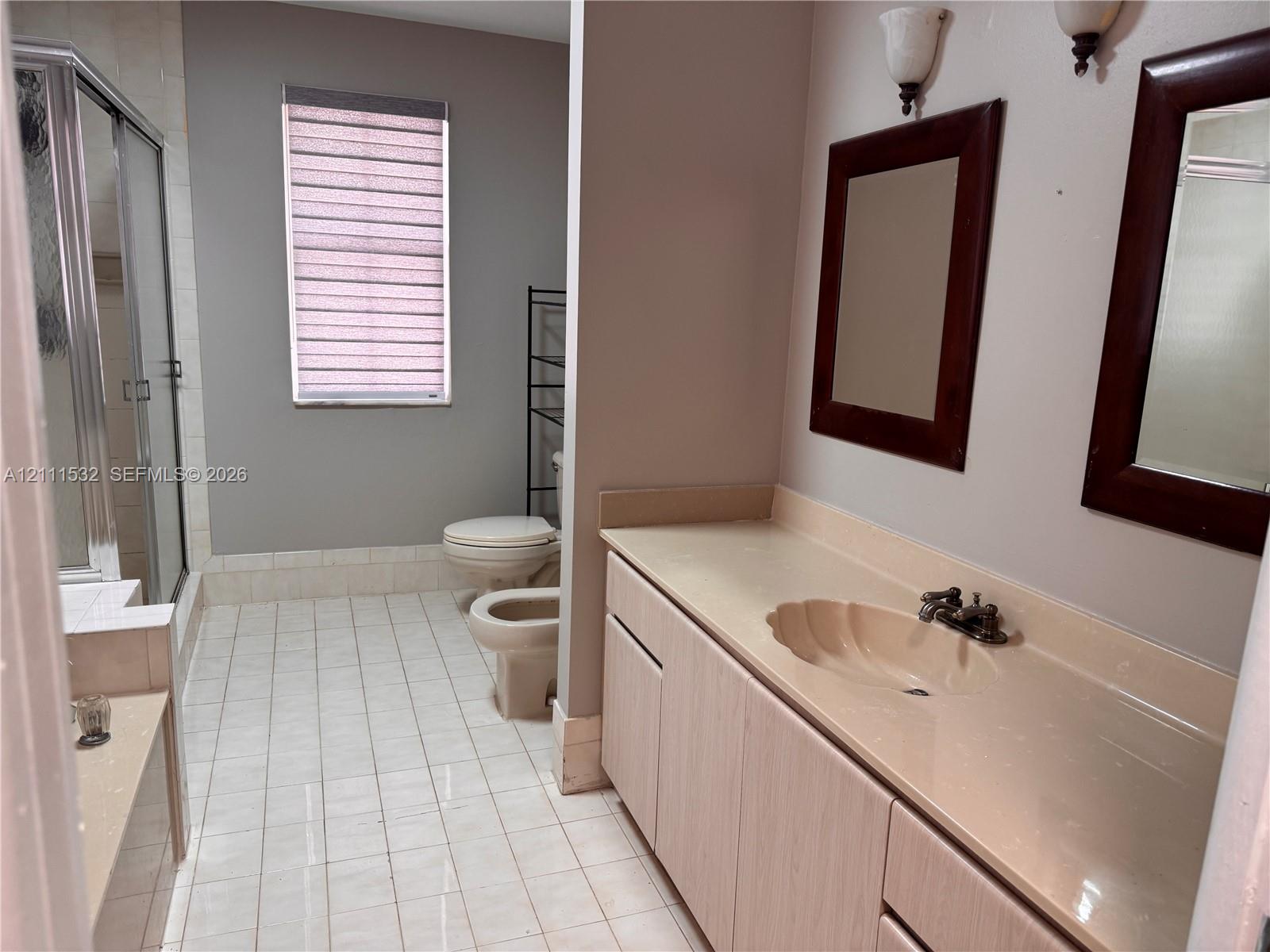 Bathroom featuring dual-sink vanity with integrated basins, tile flooring, glass-enclosed shower, and wall-mounted lighting