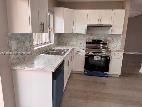 Kitchen featuring white shaker-style cabinetry, stone-patterned countertops and full-height backsplash, stainless steel range with integrated hood, stainless steel dual-basin sink, and wood-finish flooring