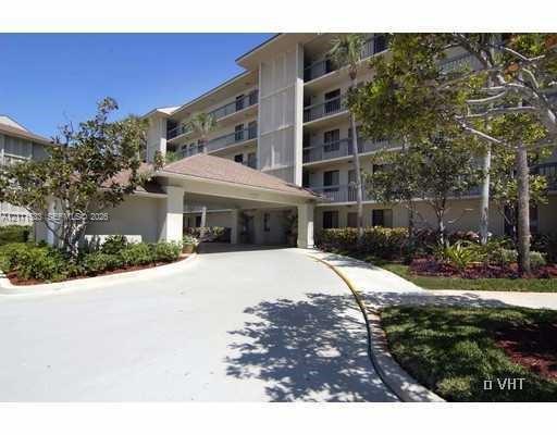 Multi-story building exterior featuring a covered porte-cochre, paved driveway, private balconies, and landscaped grounds