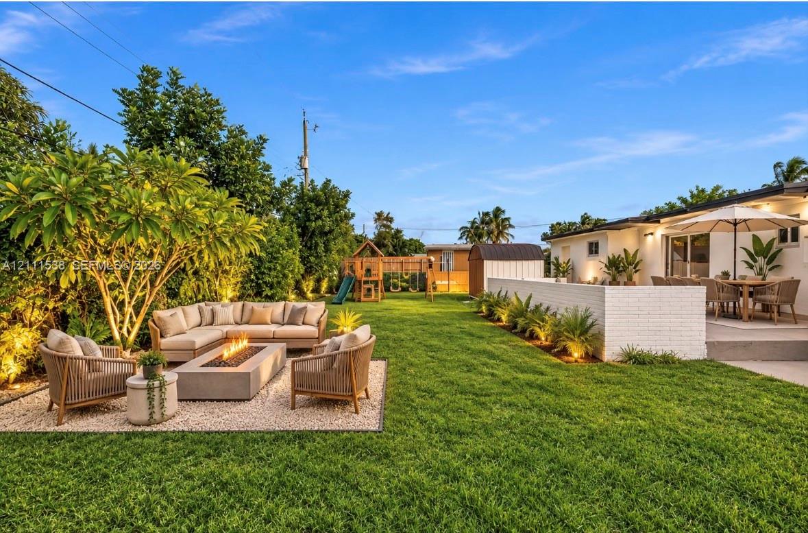 Expansive backyard featuring a manicured lawn, stone-surfaced patio area, painted brick perimeter wall, and mature landscaping