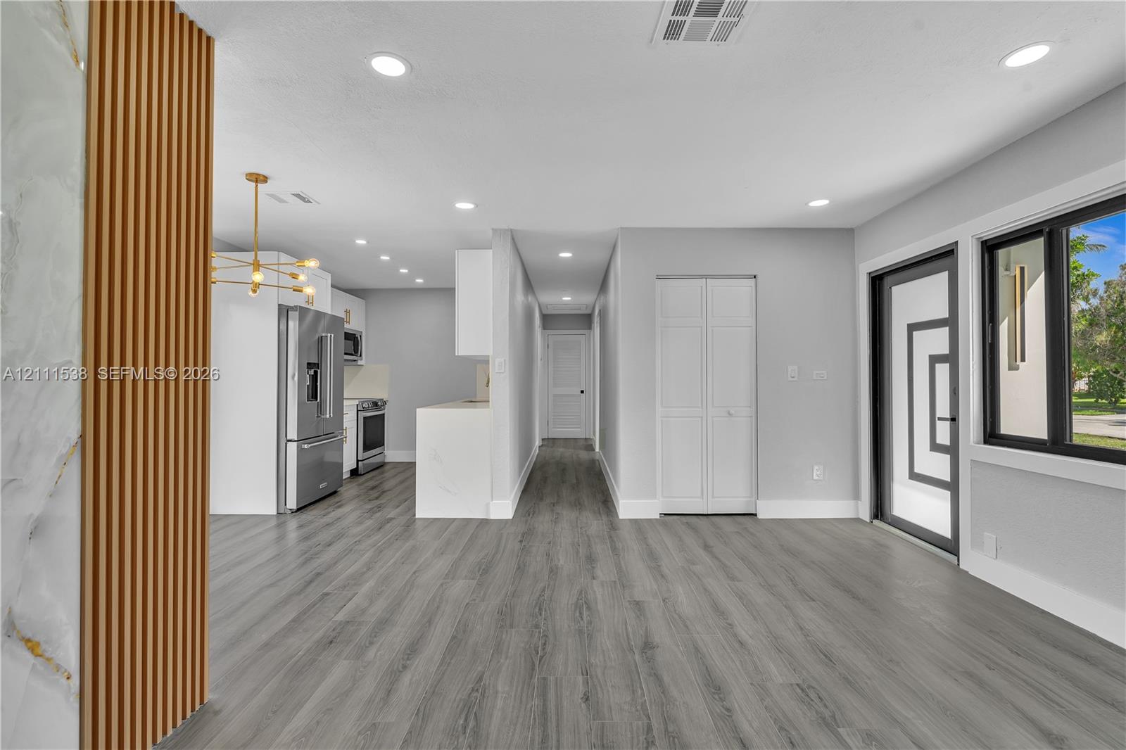 Open-concept interior featuring wood-finish flooring, recessed lighting, a modern multi-light chandelier, a stone-accented slat wall feature, and a kitchen equipped with stainless steel appliances