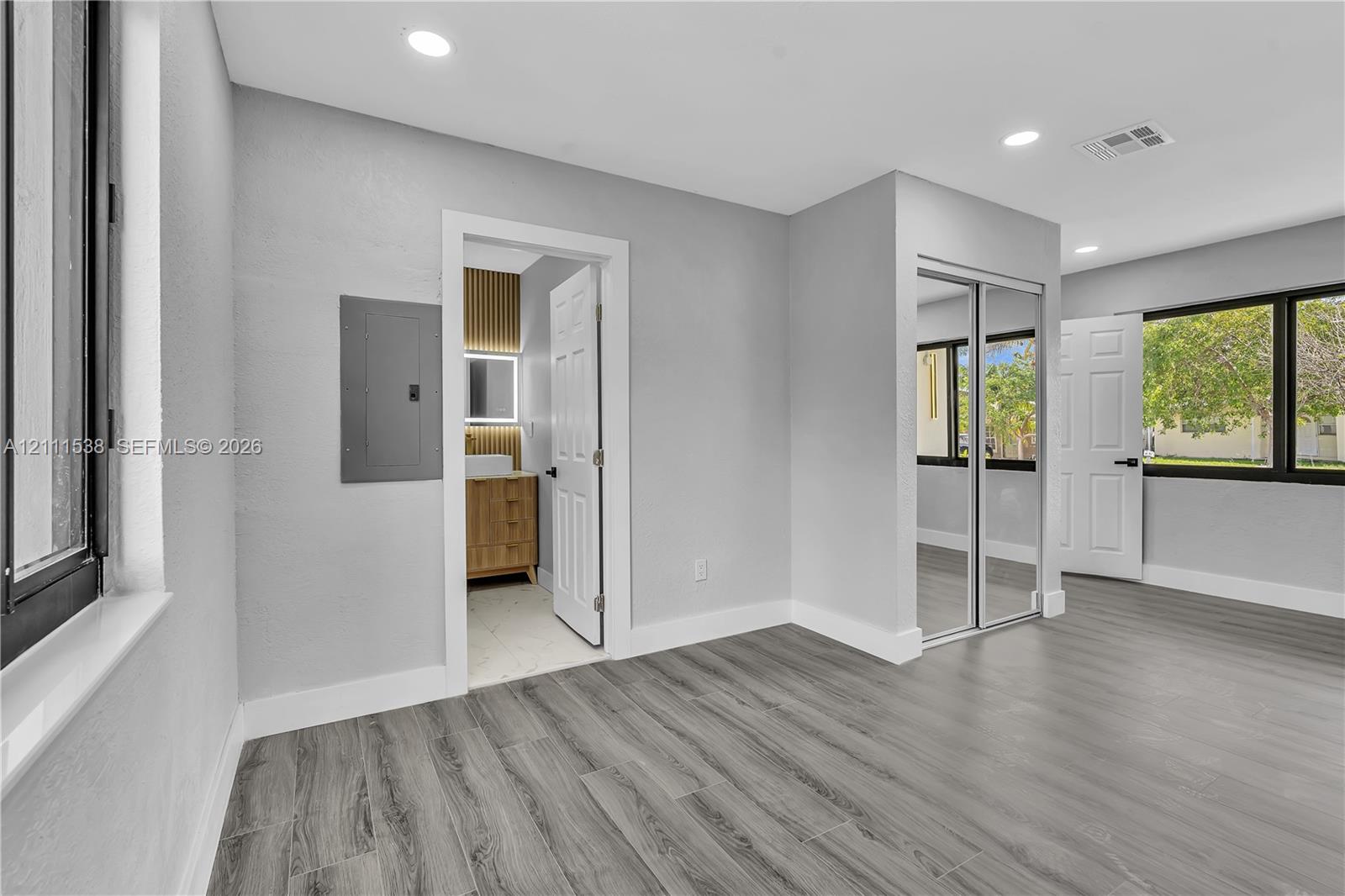 Neutral-toned interior featuring wood-finish flooring, recessed lighting, expansive multi-pane windows, and a built-in closet with sliding mirrored doors