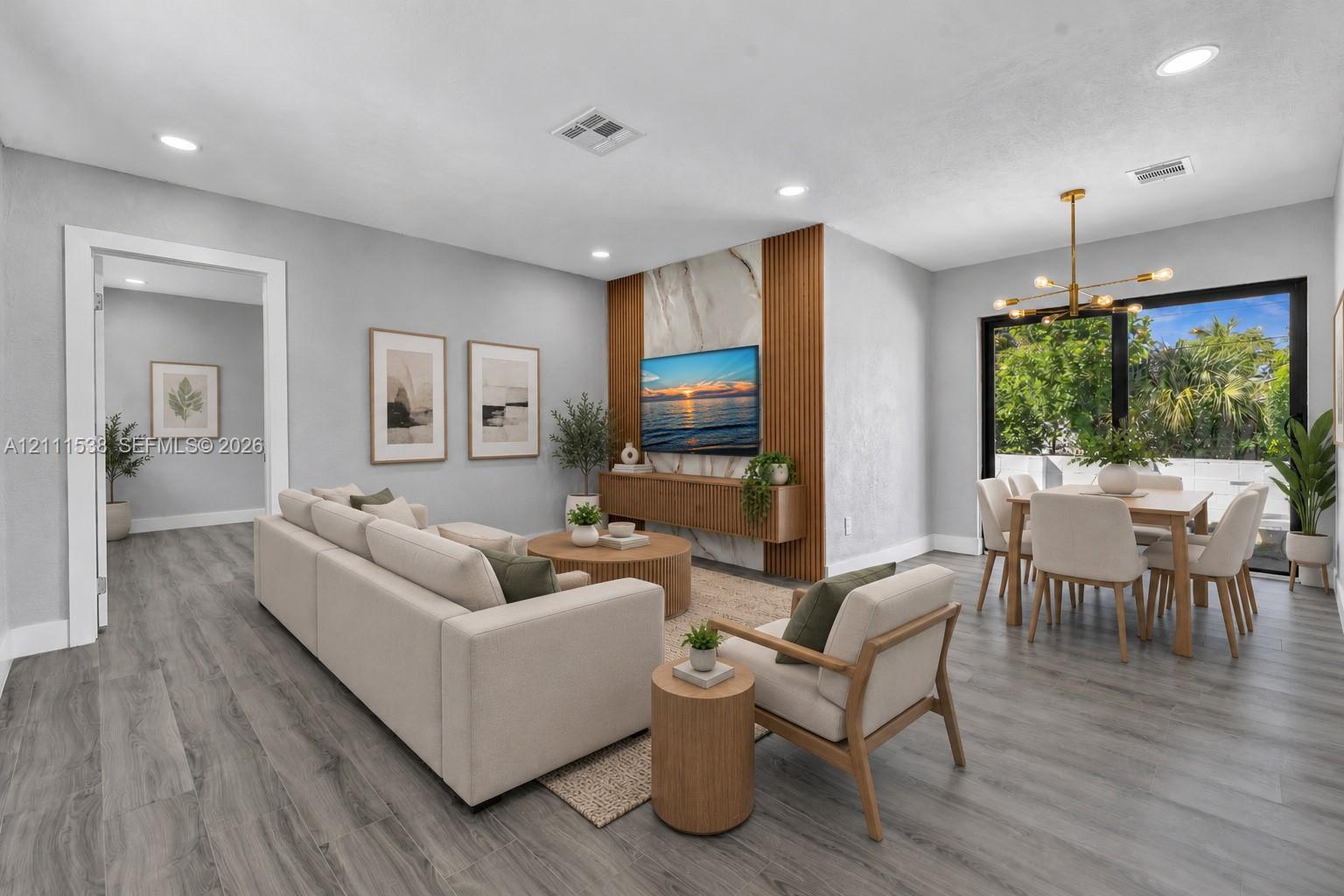 Open concept living area featuring wood-finish flooring, a floor-to-ceiling stone-tiled accent wall with vertical wood slats, a floating media console, recessed lighting, and a modern multi-arm chandelier