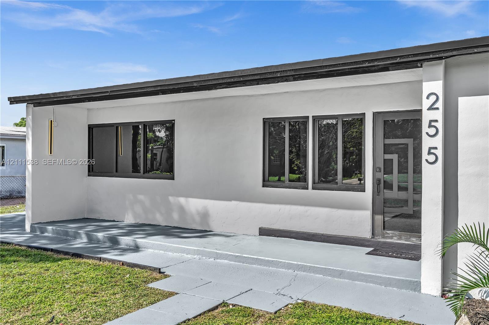 Exterior facade featuring a clean white finish, dark-framed windows, a covered concrete porch, and a glass-paneled entry door