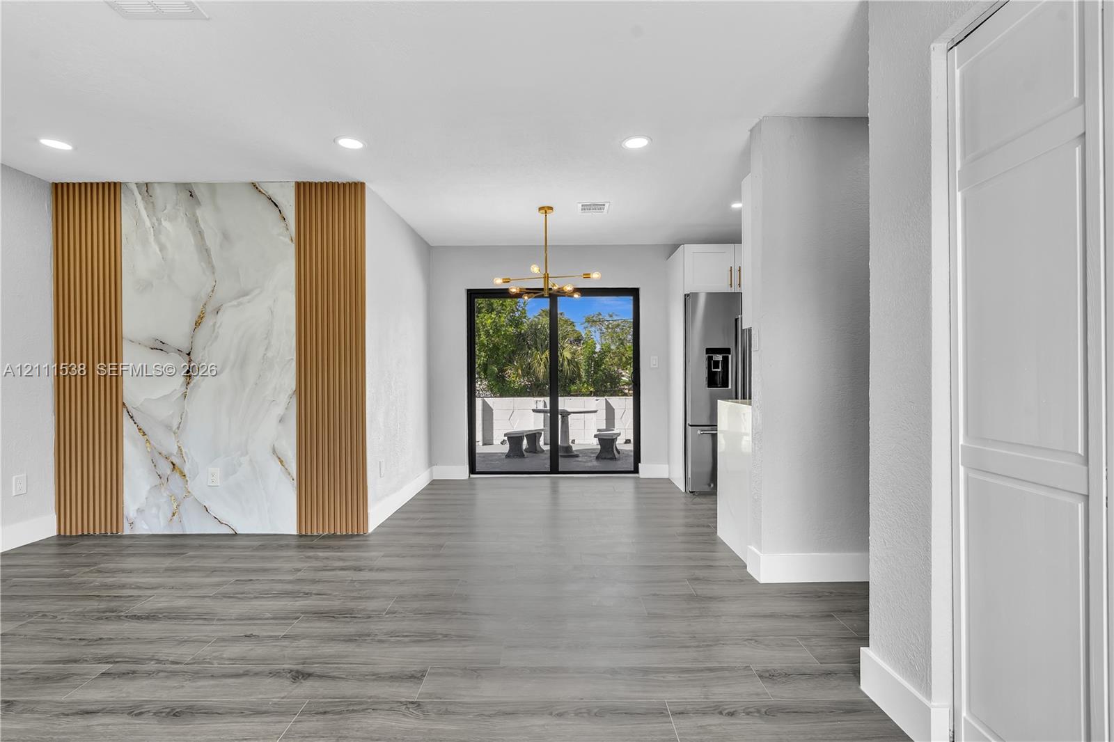 Large-format wall accent featuring stone-finish slab and vertical wood slats, wood-finish flooring, recessed lighting, multi-arm metal chandelier, and sliding glass patio doors