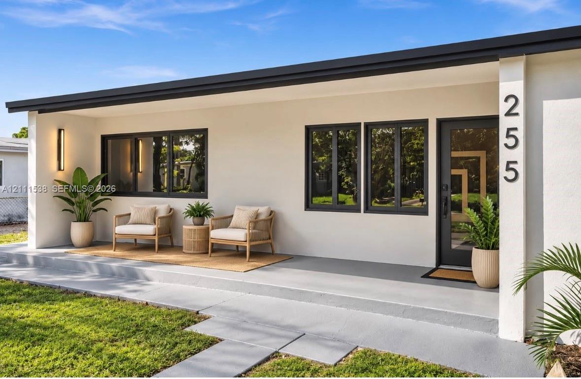 Exterior featuring smooth white stucco finish, dark-framed windows, integrated exterior wall sconce, concrete porch, and front entry door with glass panel Exterior featuring smooth white stucco finish, dark-framed windows, integrated exterior wall sconce, concrete porch, and front entry door with glass panel