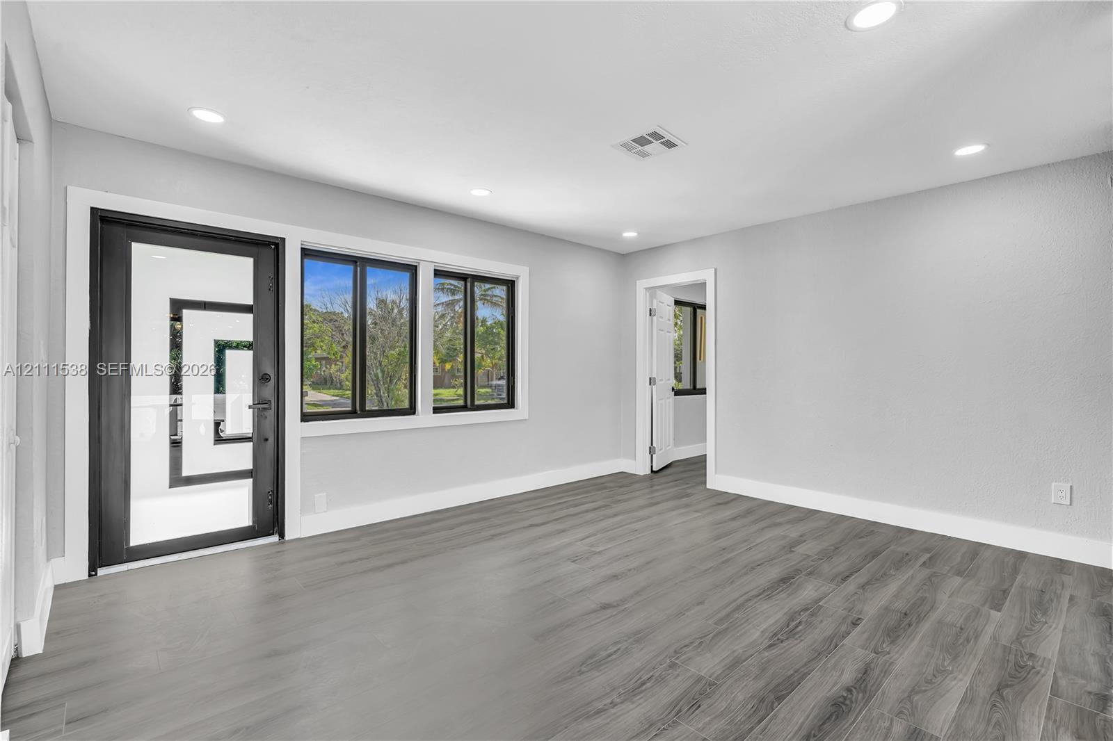 Interior space featuring wood-finish flooring, recessed lighting, a full-glass entry door with a dark frame, and multi-pane windows with dark casing