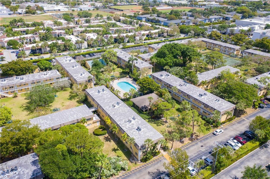 Aerial perspective of the residential complex featuring multi-story structures, an outdoor swimming pool, paved parking areas, and mature landscaping