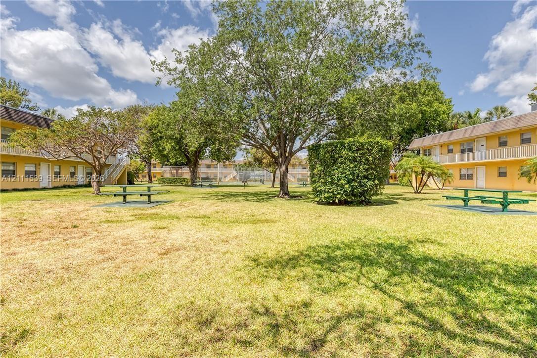 Common grounds featuring a grass lawn, mature trees, manicured hedges, and exterior building structures