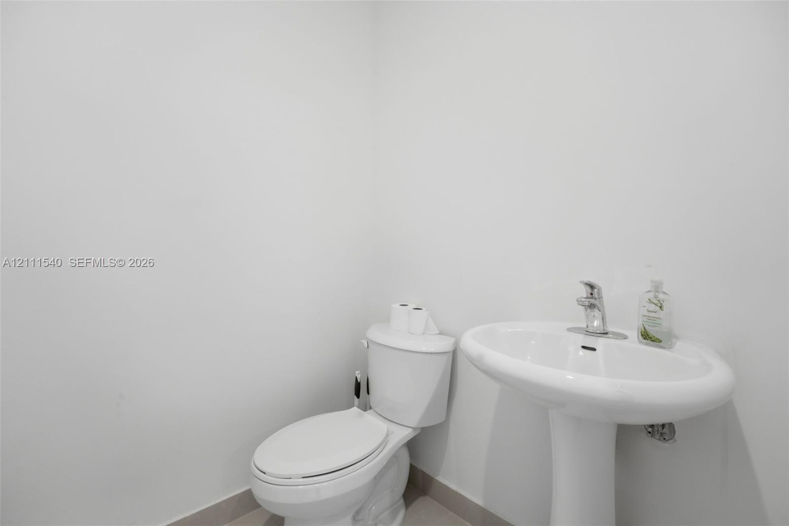 White pedestal sink with a polished chrome faucet and matching white toilet