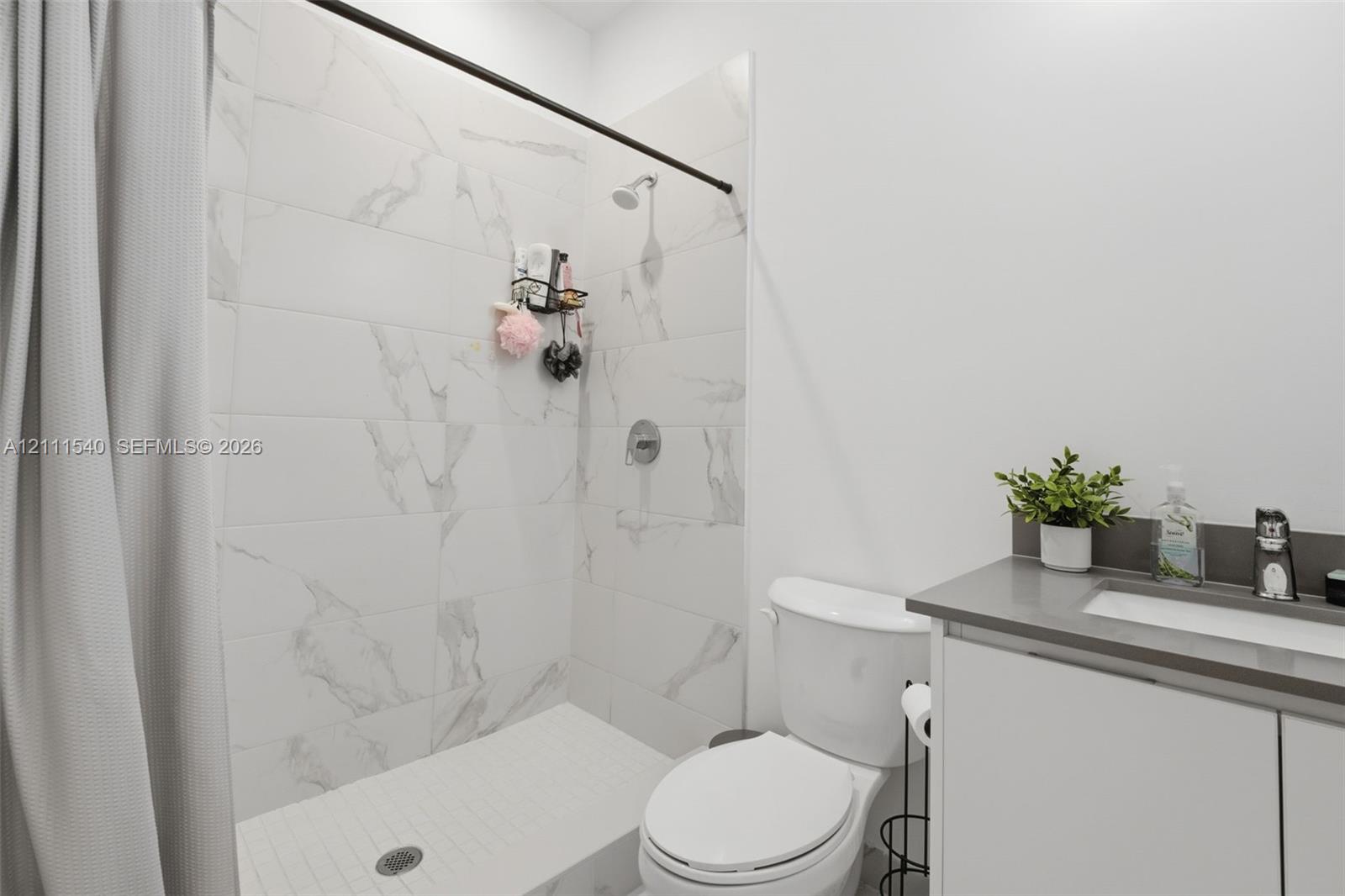 Shower enclosure featuring large-format veined tile surround, matte black shower hardware, and vanity with stone-finish countertop and integrated sink