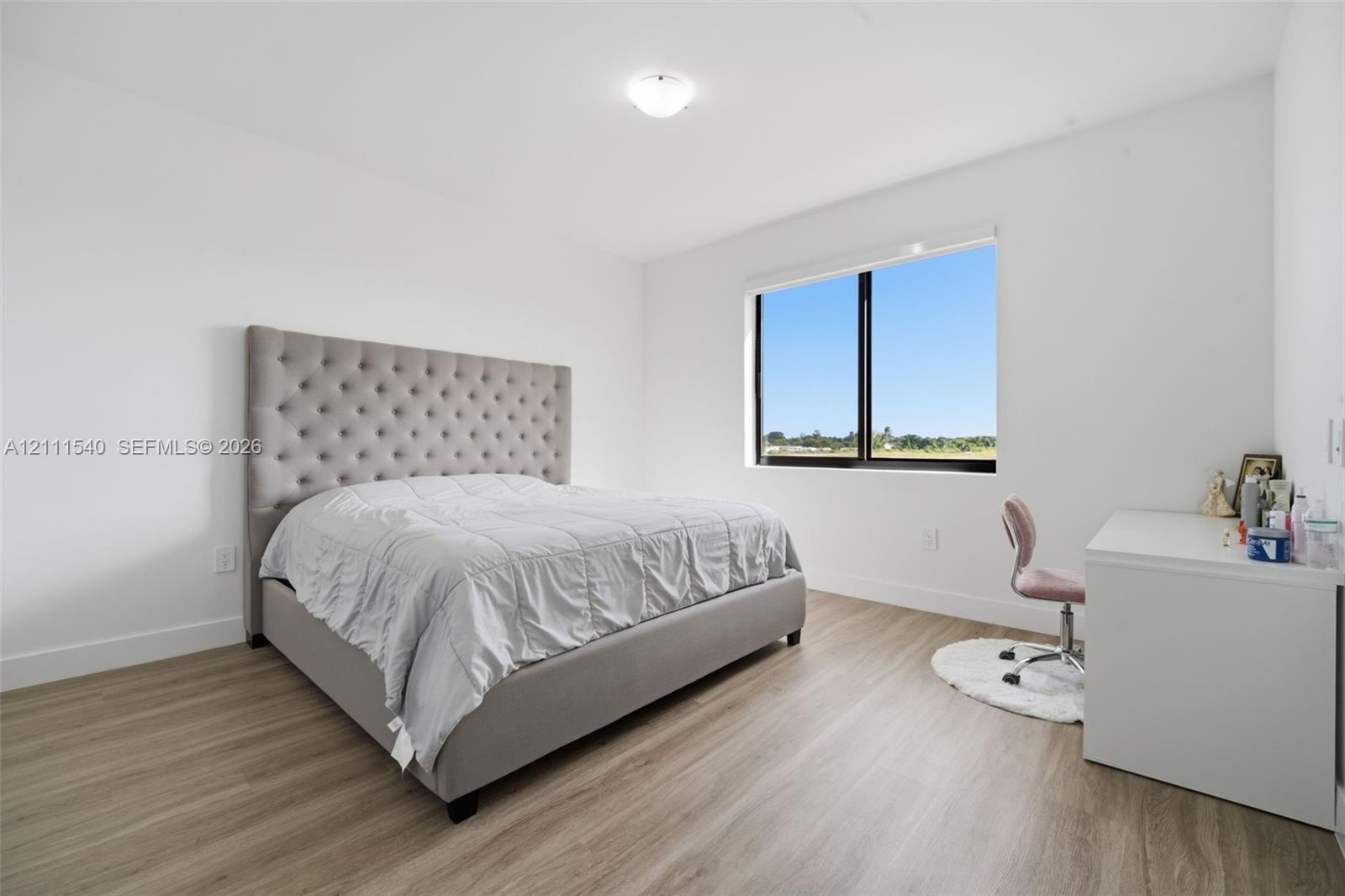 Neutral-toned wood-finish flooring, white walls, and large window with dark trim