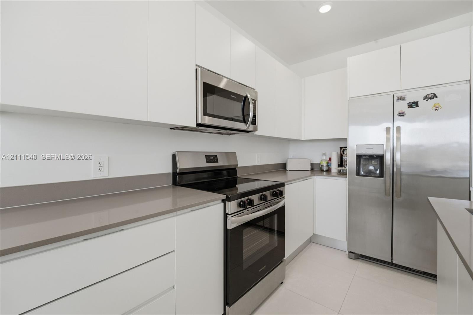 Kitchen featuring flat-panel white cabinetry, solid-surface countertops, recessed lighting, and stainless steel appliances including a range, microwave, and refrigerator