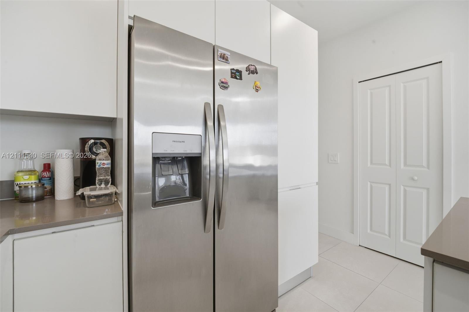 Stainless steel side-by-side refrigerator, flat-panel white cabinetry, solid-surface countertops, and light-colored tile flooring