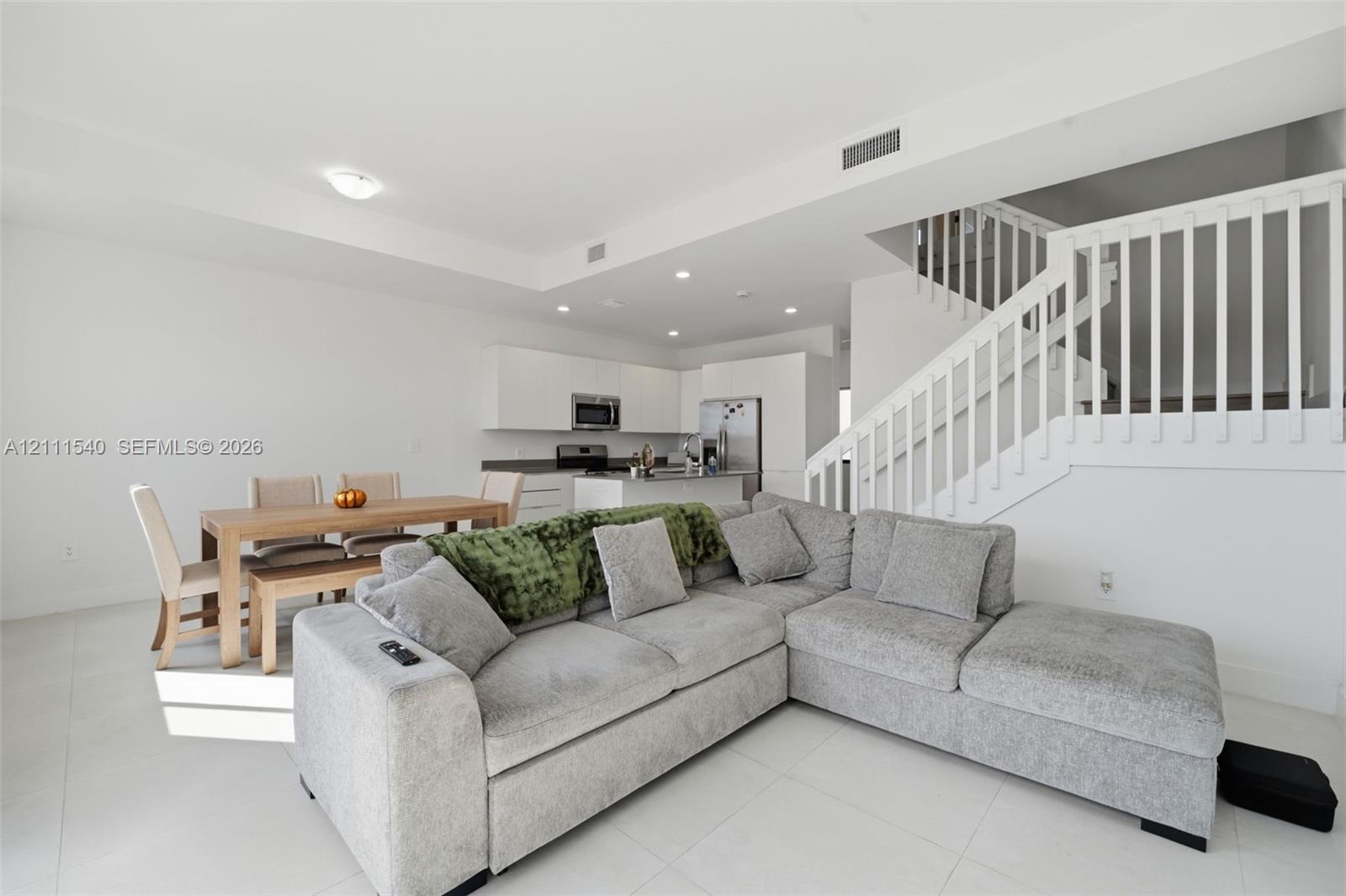 Open-concept living space featuring neutral tile flooring, recessed lighting, and a staircase with white vertical balusters