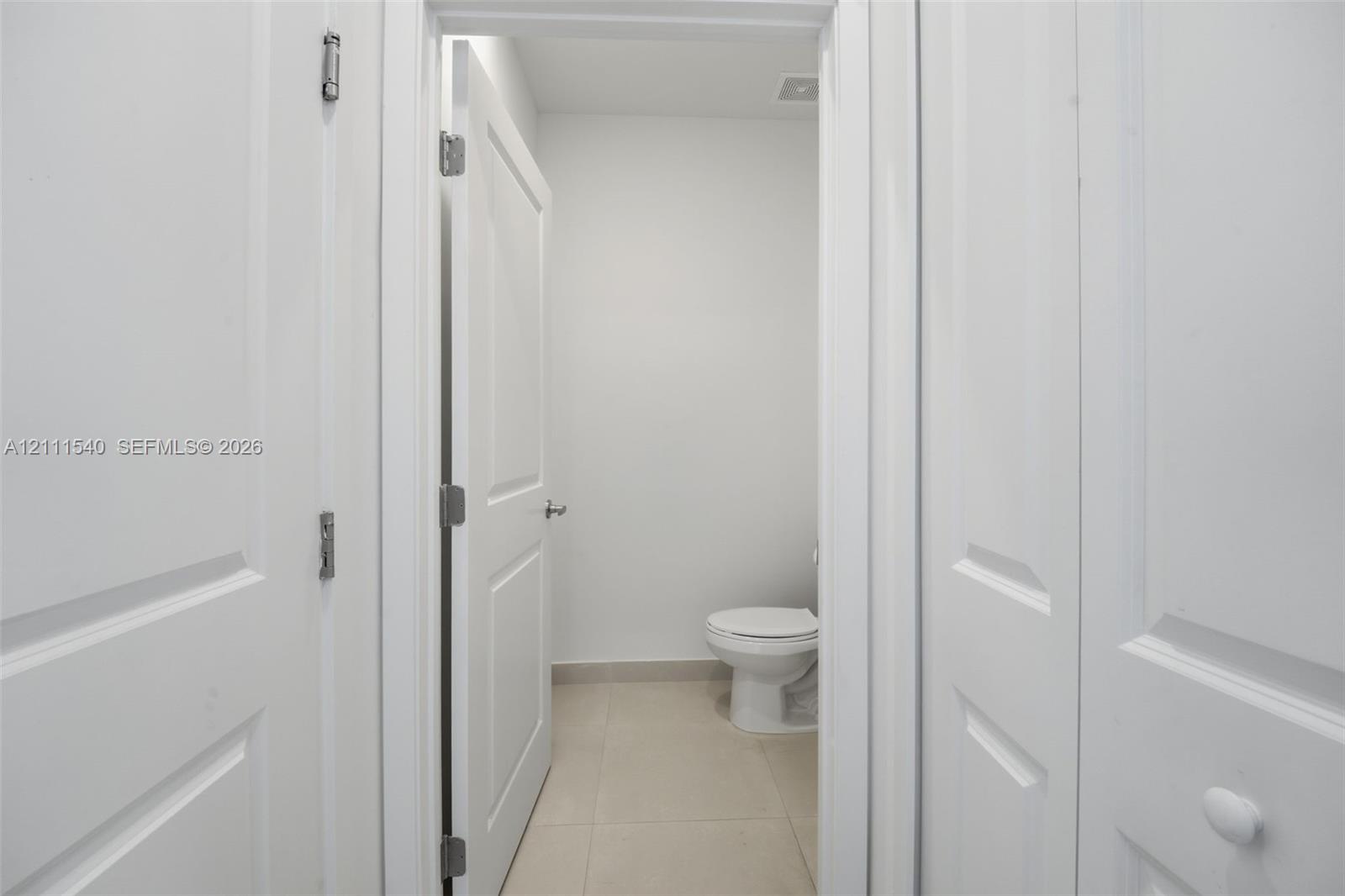 Neutral interior featuring white two-panel doors, neutral large-format floor tile, and a porcelain toilet