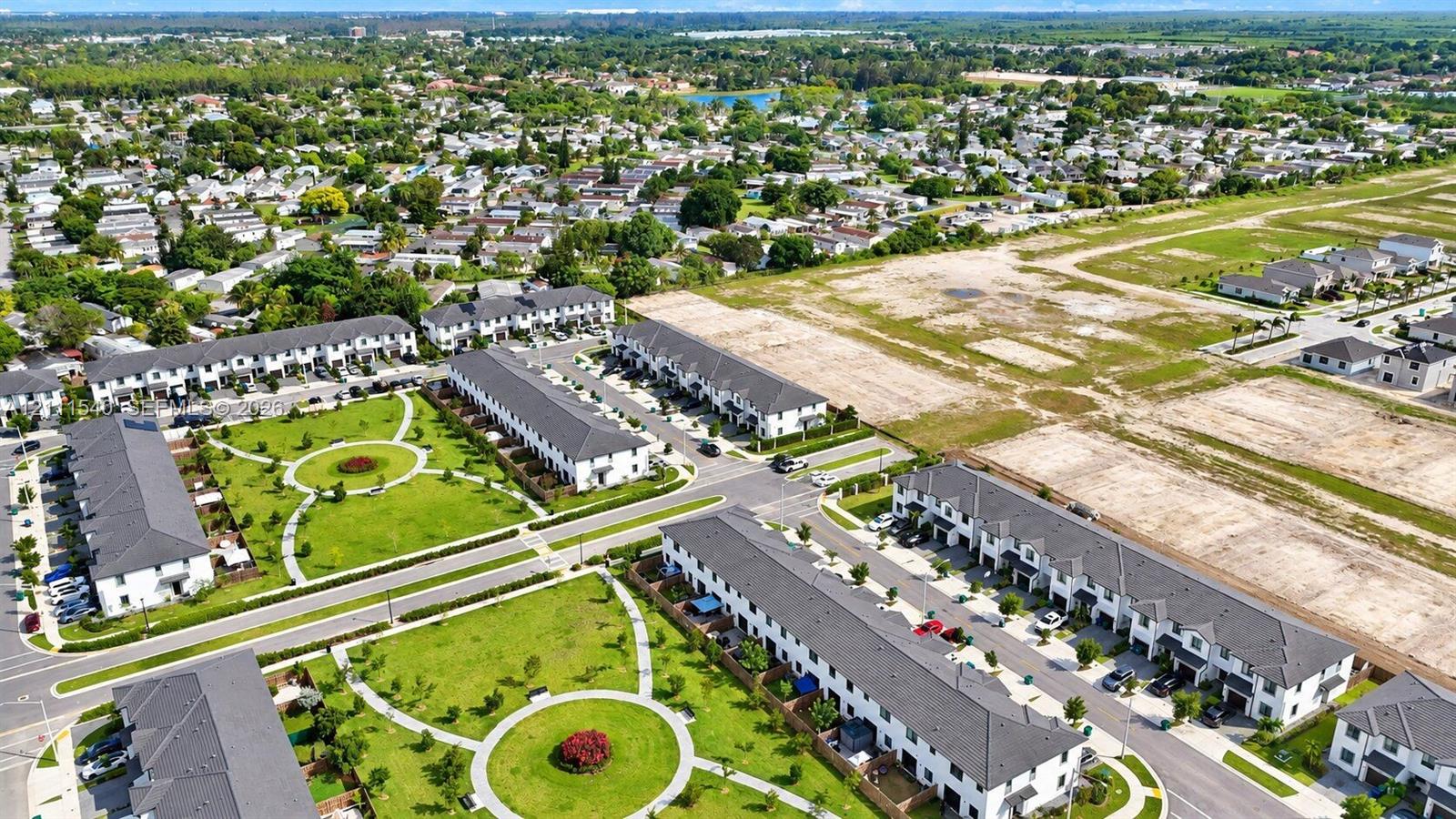 Aerial perspective of a multi-unit residential community featuring paved thoroughfares, interconnected walking paths, landscaped green spaces, and uniform architectural design