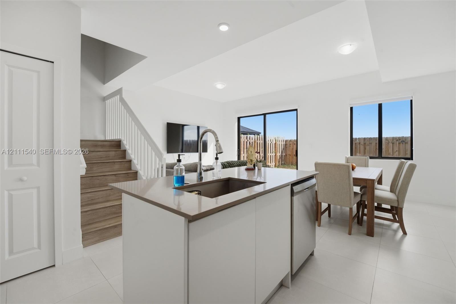 Kitchen island with stone-surface countertop, stainless steel undermount sink, wood-finish stairs with white railing, and sliding glass doors