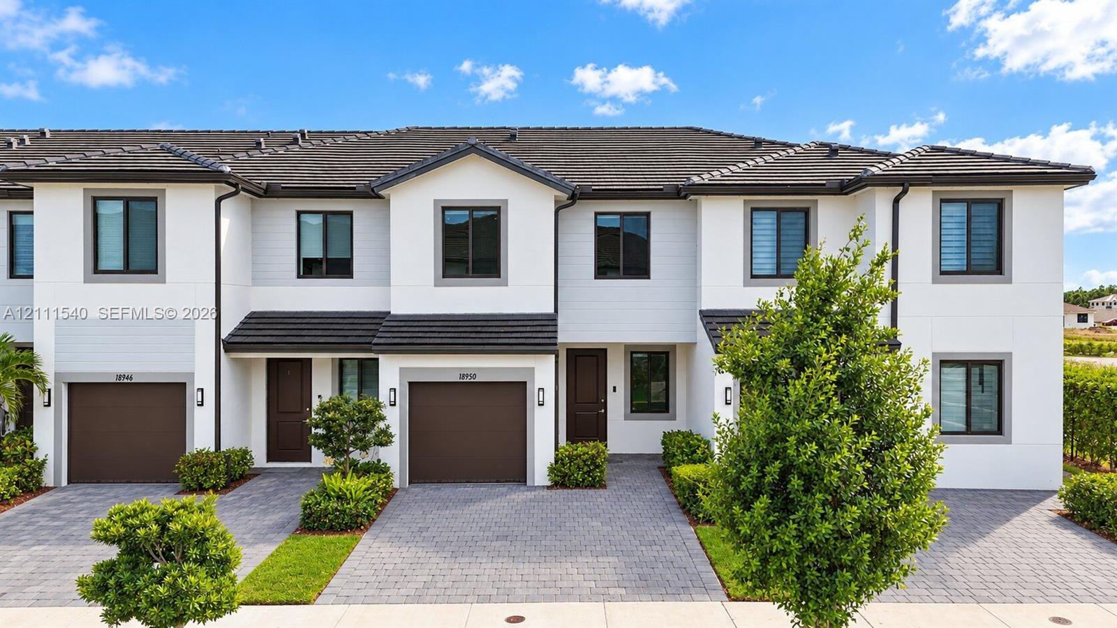Multi-story townhome exterior featuring crisp white siding, dark-toned tile roofing, paved driveways, and attached garage entries