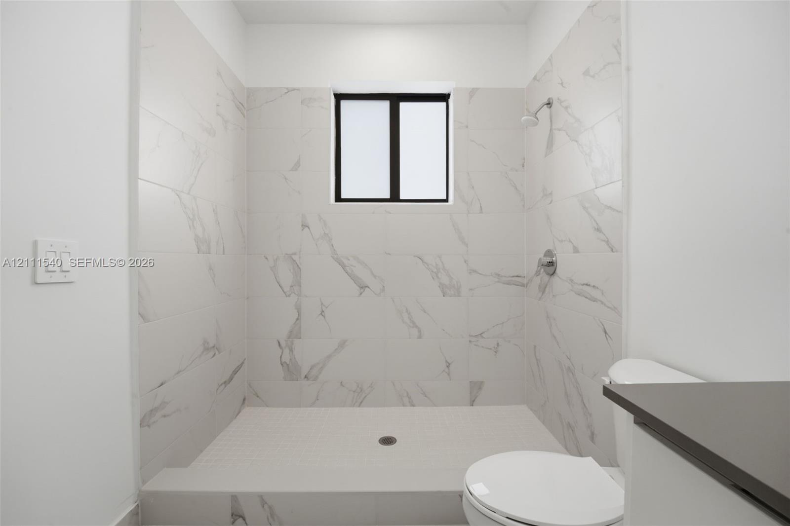 Walk-in shower featuring floor-to-ceiling stone-finish tile surround, a built-in shower head, and a privacy window