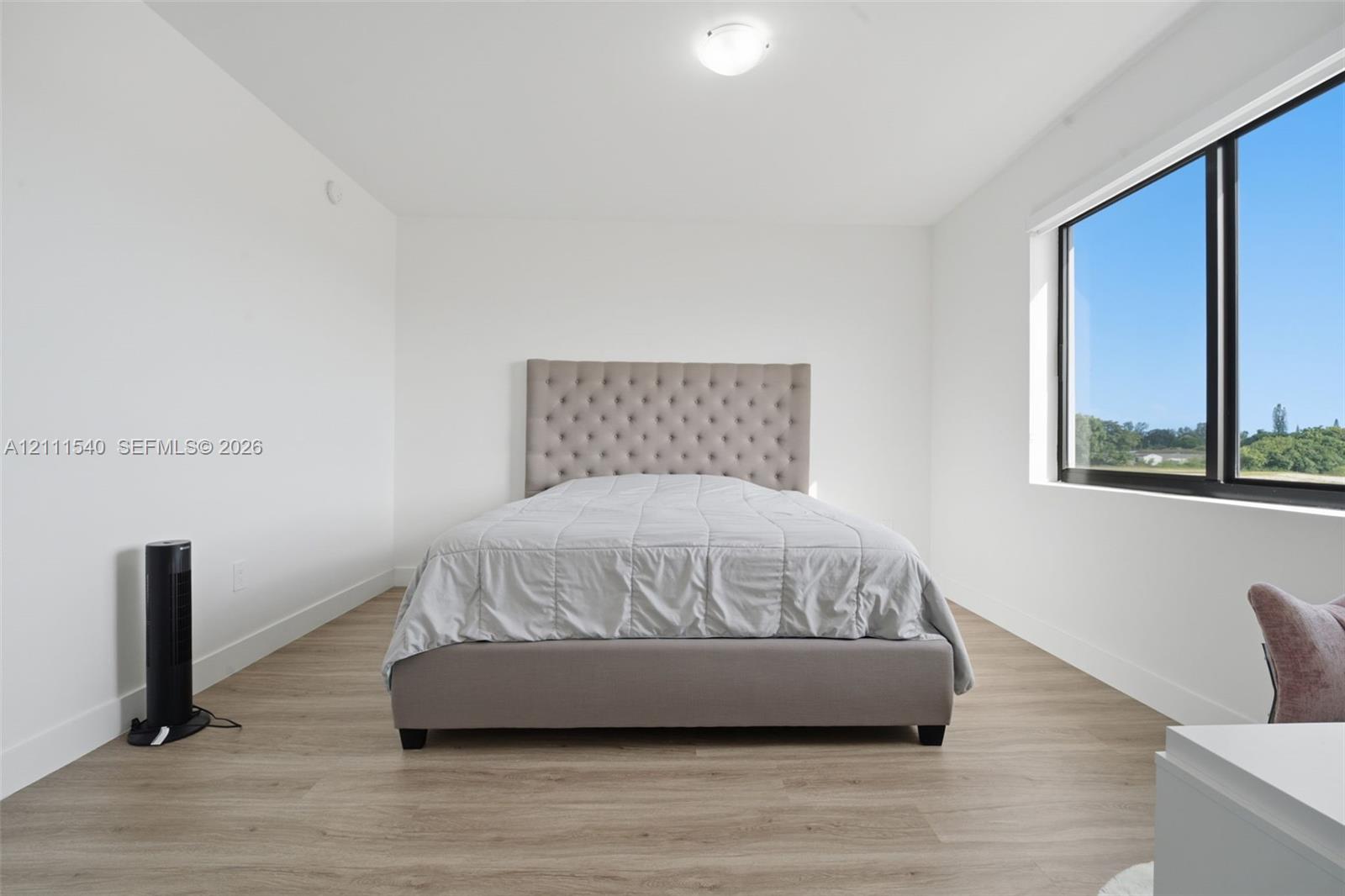 Minimalist room featuring white walls, wood-finish flooring, and a large window