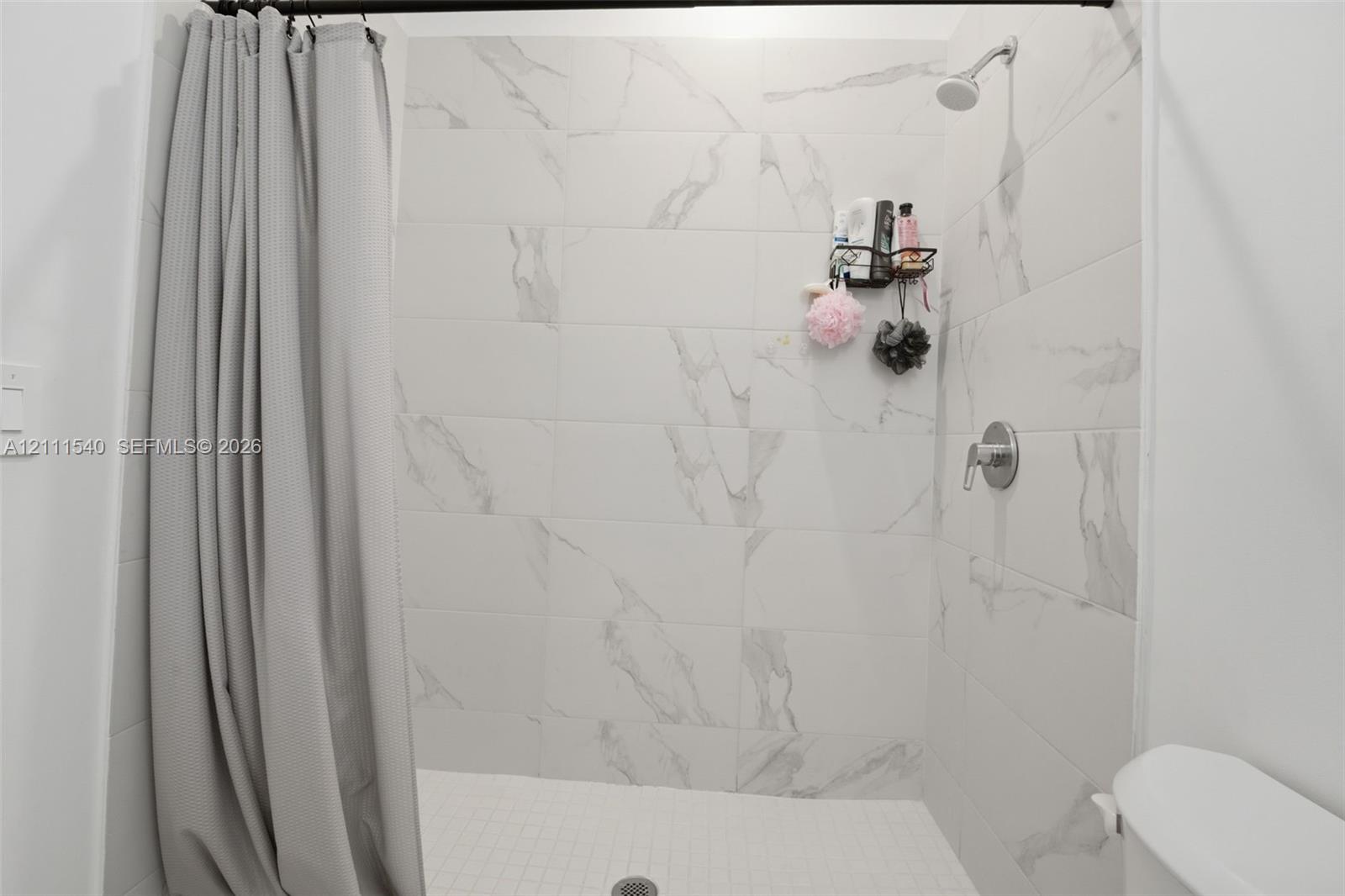 Shower enclosure featuring large-format light-toned stone-finish wall tile with prominent veining, a wall-mounted showerhead, and a single-handle pressure balance valve