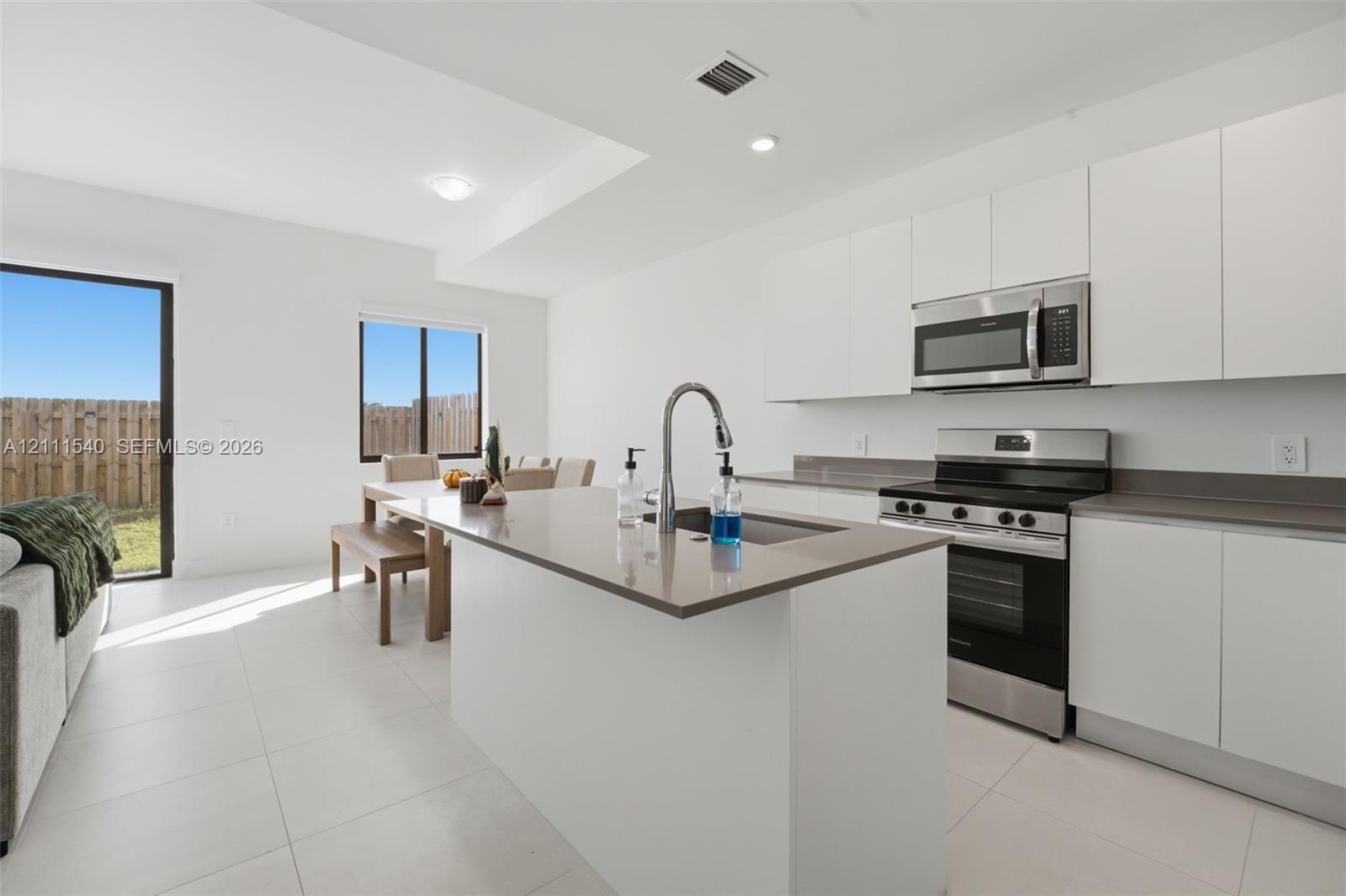 Modern kitchen featuring matte white slab-front cabinetry, neutral-toned solid surface countertops, a central island with an undermount stainless steel sink, and stainless steel appliances