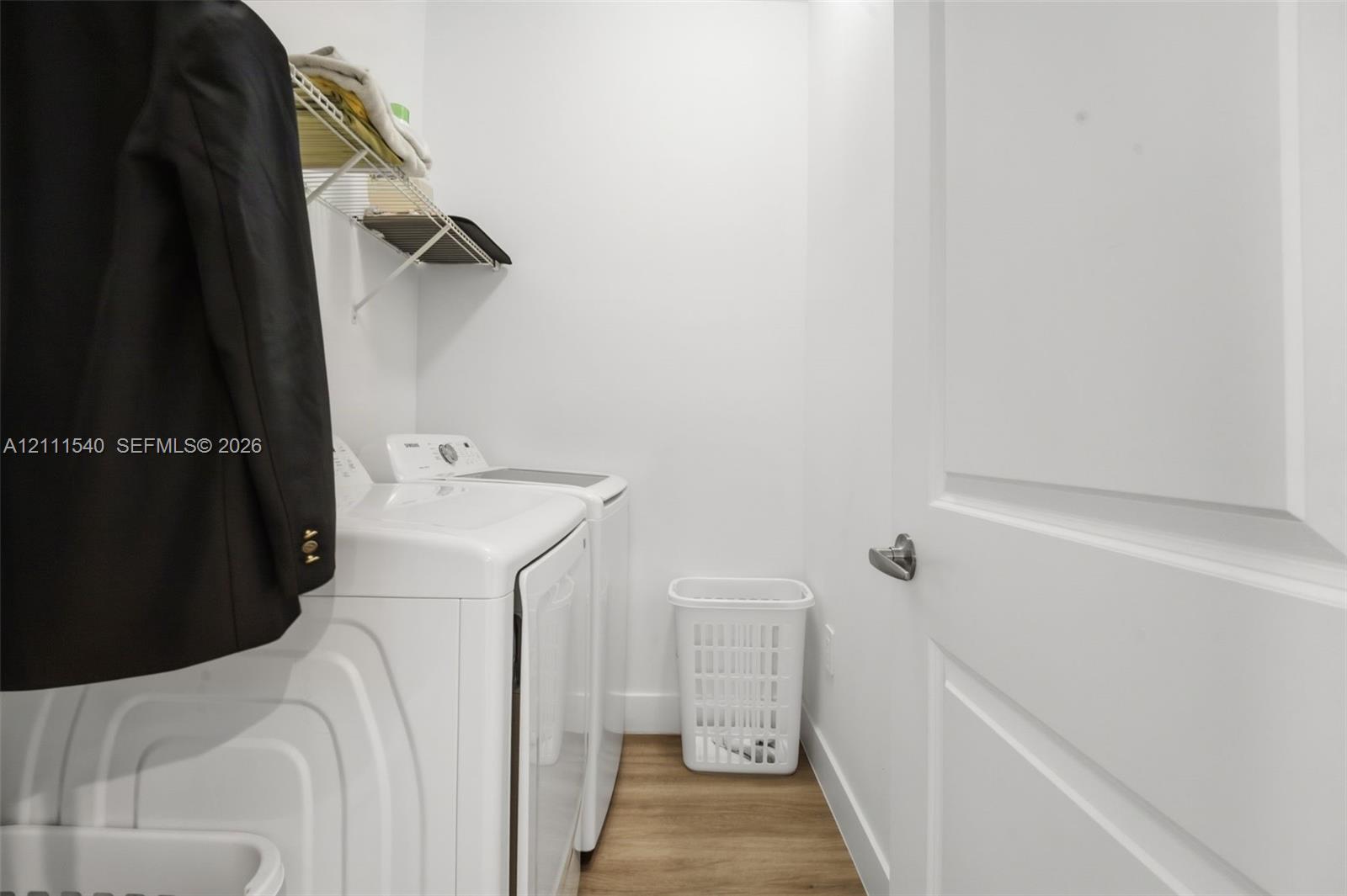 Dedicated laundry space featuring wood-finish flooring, white paneled door, and wire wall-mounted shelving
