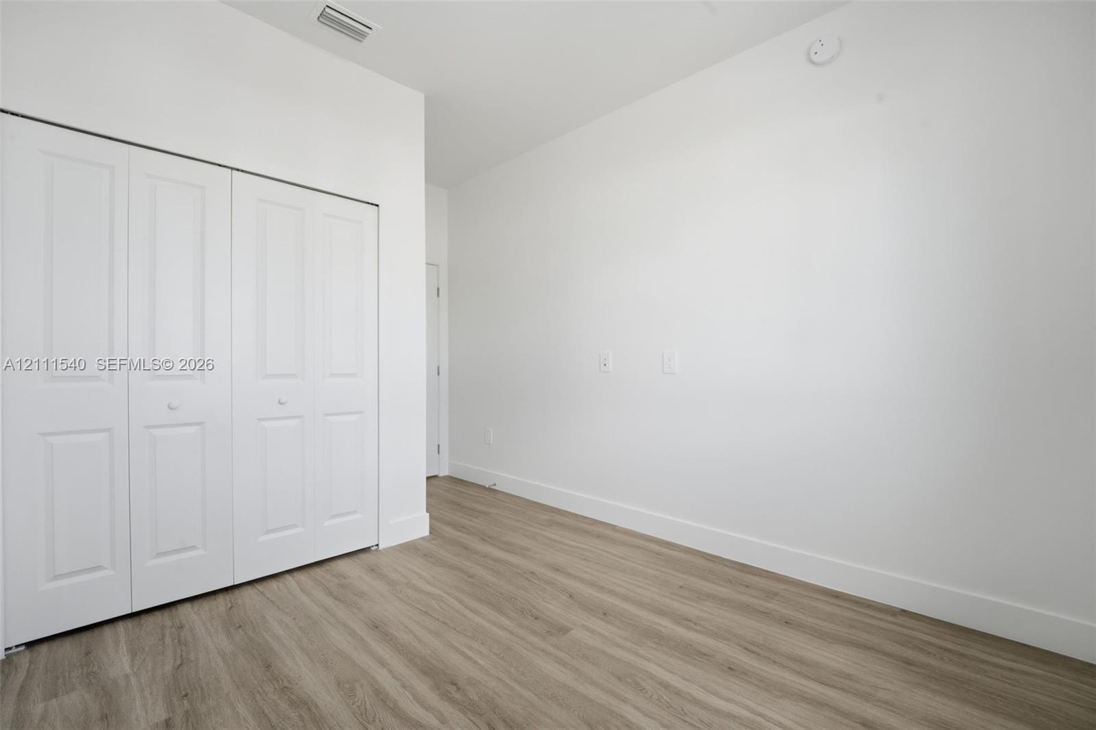Room featuring wood-finish flooring, white walls, and a white bi-fold closet door