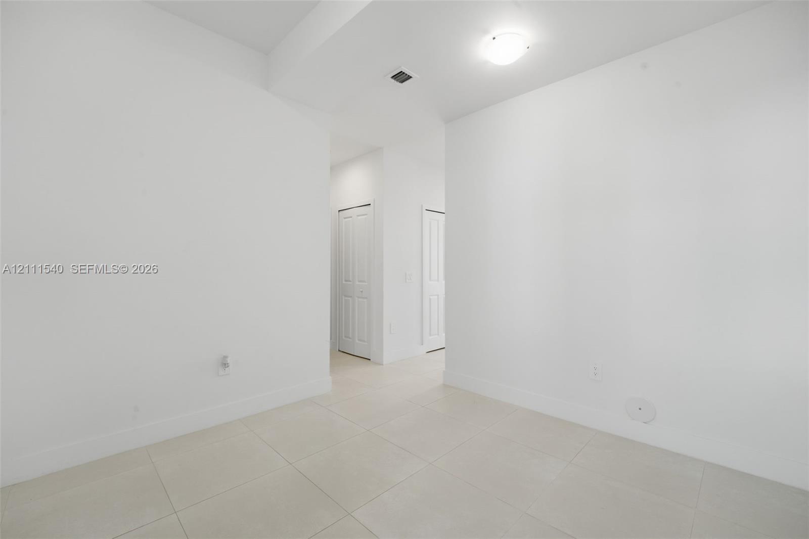 Neutral interior space featuring large-format ceramic tile flooring, crisp white walls, and two multi-panel interior doors