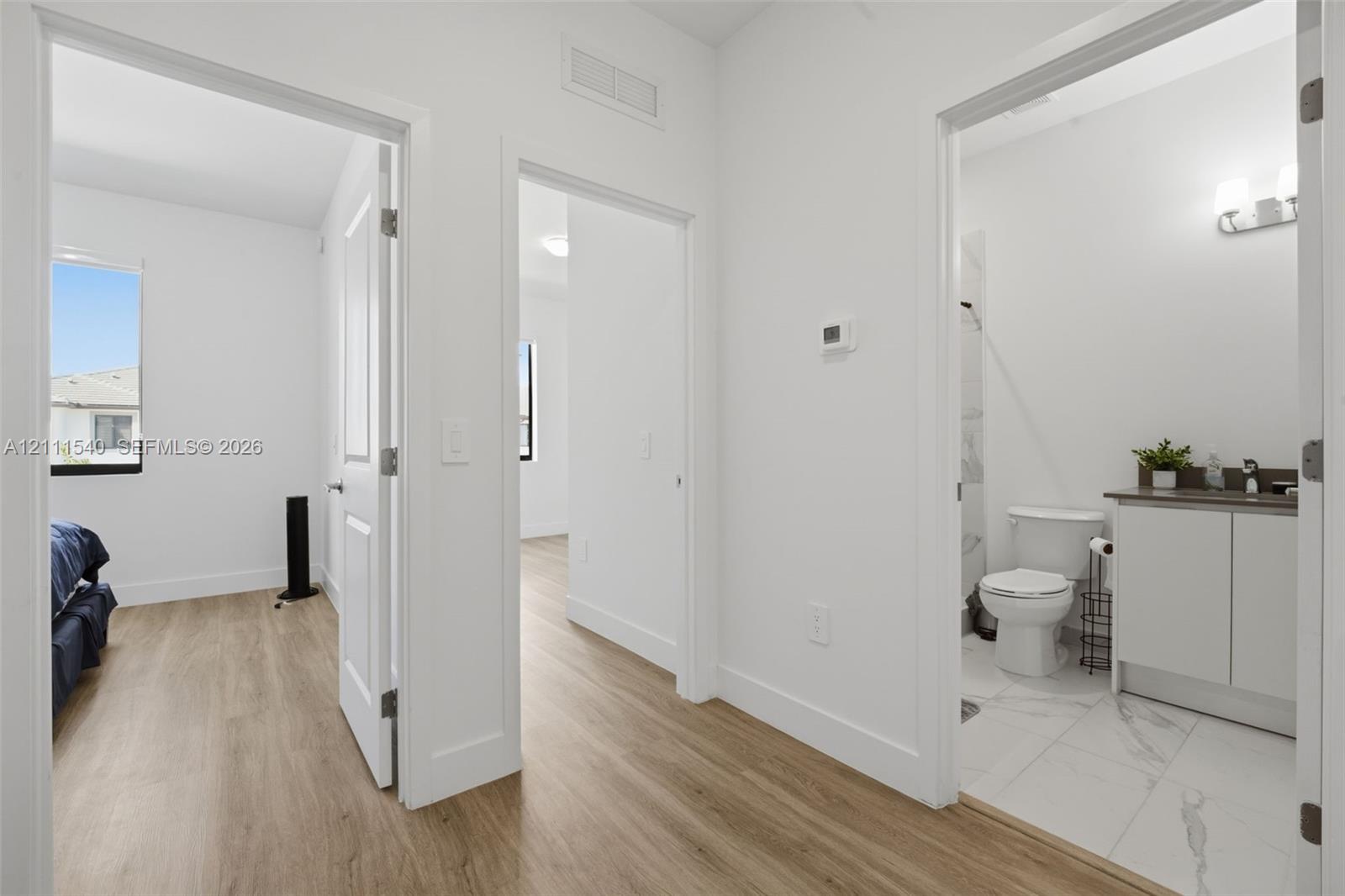 Wood-finish flooring throughout, white interior doors, and a bathroom featuring a vanity with a countertop, a wall-mounted light fixture, and tile flooring
