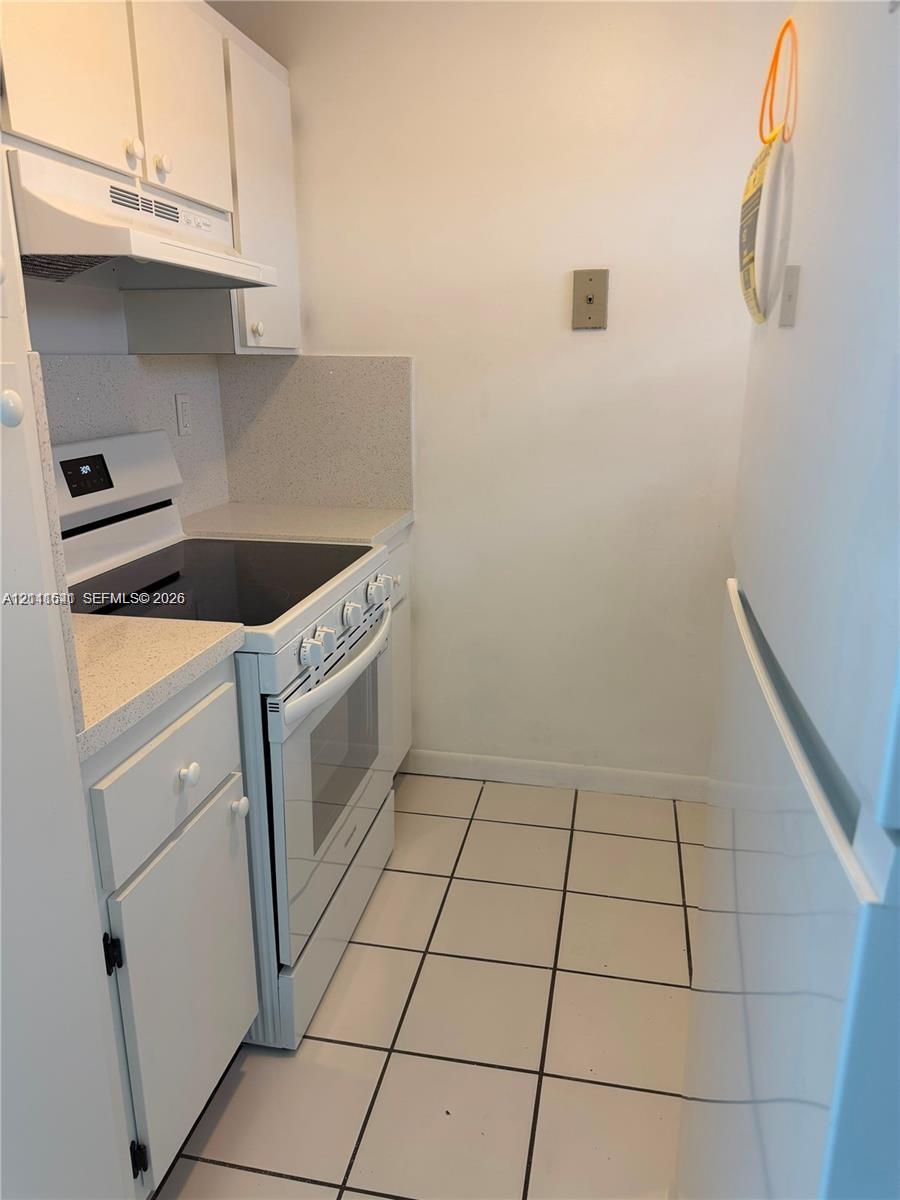 Kitchen featuring white cabinetry, solid-surface countertops, electric range, range hood, and tile flooring Kitchen featuring white cabinetry, solid-surface countertops, electric range, range hood, and tile flooring