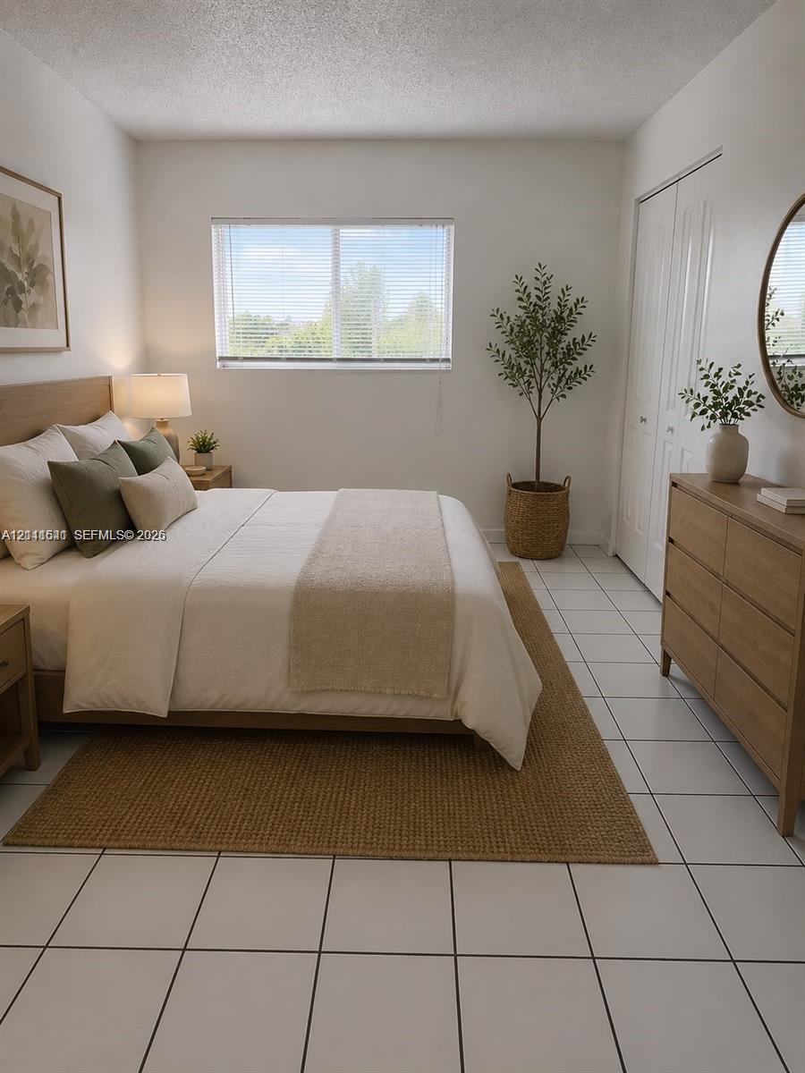 Room featuring light-colored tile flooring, a large window with blinds, and double-door closet storage Room featuring light-colored tile flooring, a large window with blinds, and double-door closet storage
