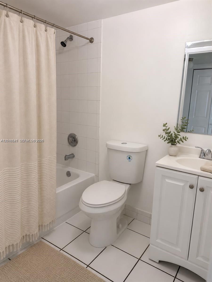 Bathroom featuring white tiled flooring, a bathtub with white tile surround, a single-sink vanity with white cabinetry, and a wall-mounted mirror Bathroom featuring white tiled flooring, a bathtub with white tile surround, a single-sink vanity with white cabinetry, and a wall-mounted mirror