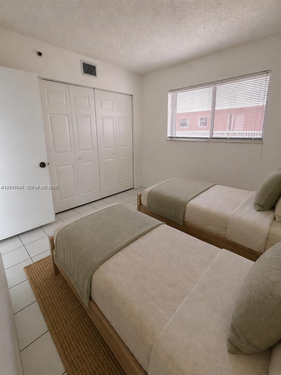Neutral-toned room featuring ceramic tile flooring, a large window with horizontal blinds, and a built-in multi-panel closet Neutral-toned room featuring ceramic tile flooring, a large window with horizontal blinds, and a built-in multi-panel closet