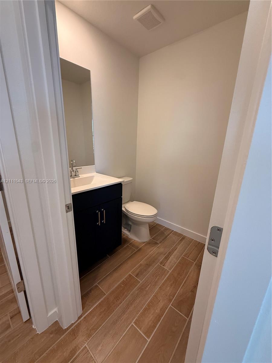 Dark-finish vanity cabinet, solid-surface countertop with integrated sink, polished chrome faucet, tall vertical wall mirror, and wood-finish flooring